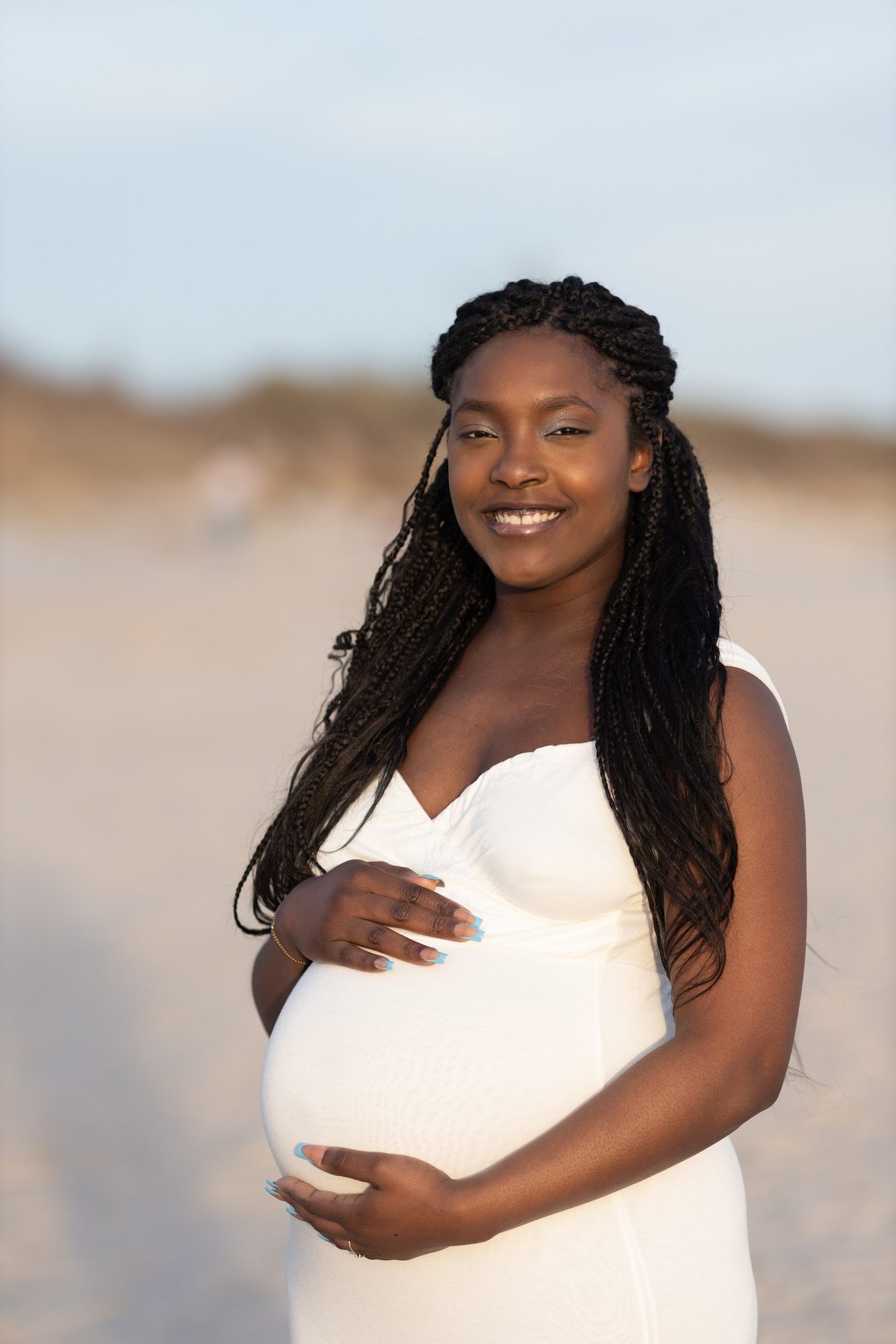 Partner cradling the bump on the sand — coastal maternity portrait