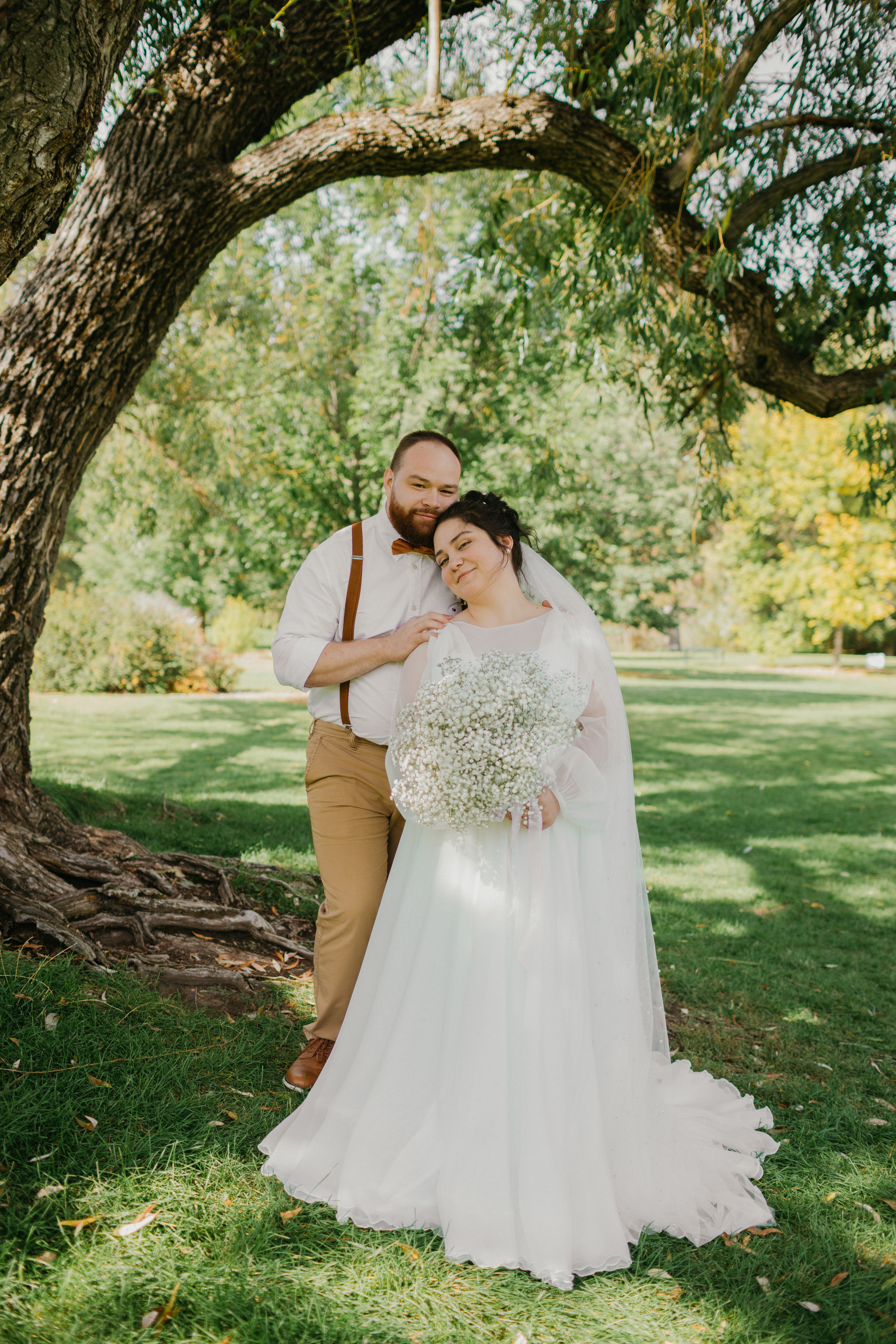 Bride and groom laughing beneath a willow tree with baby's breath bouquet