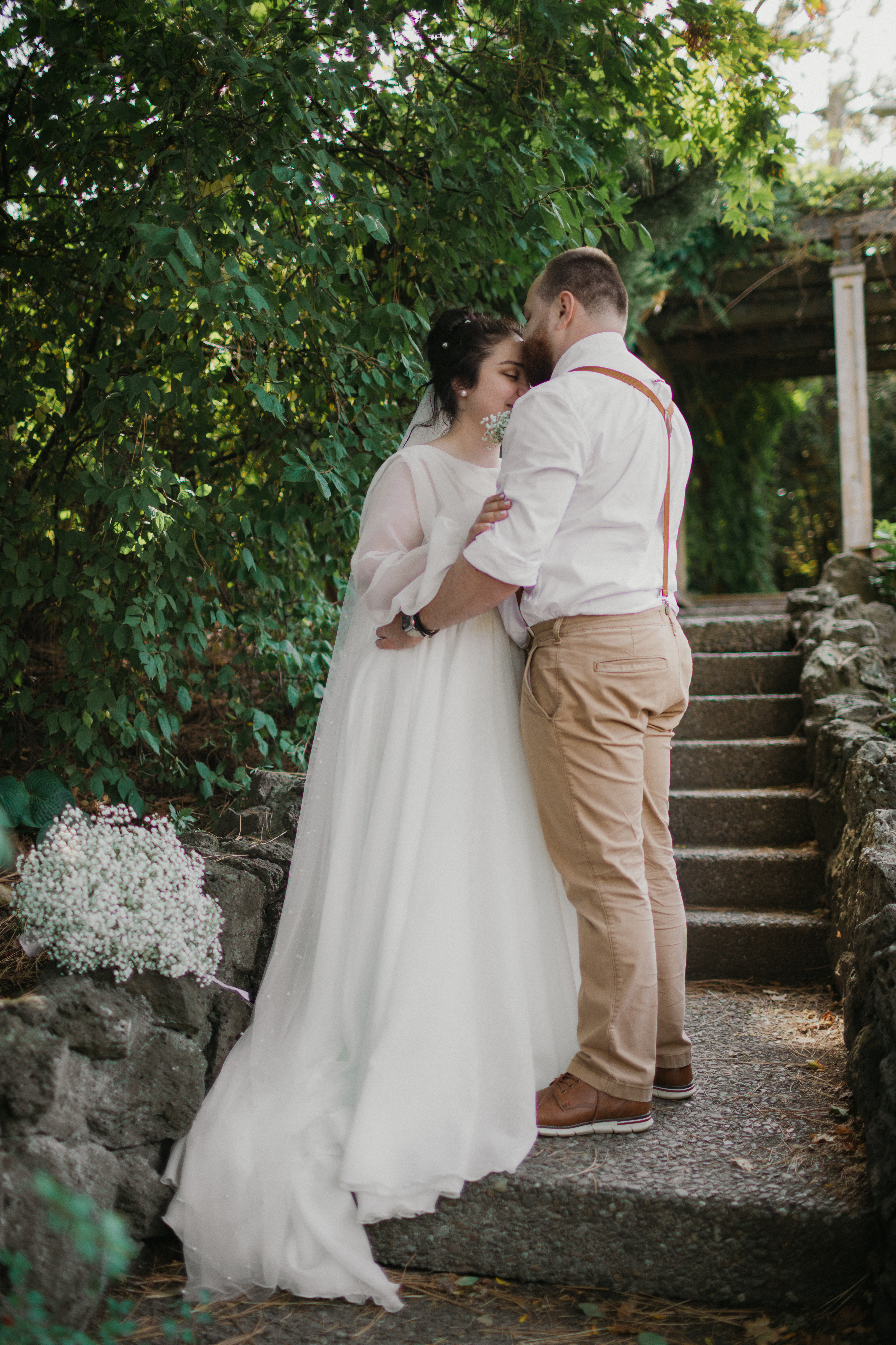Bride and groom embrace on stone garden steps beneath greenery