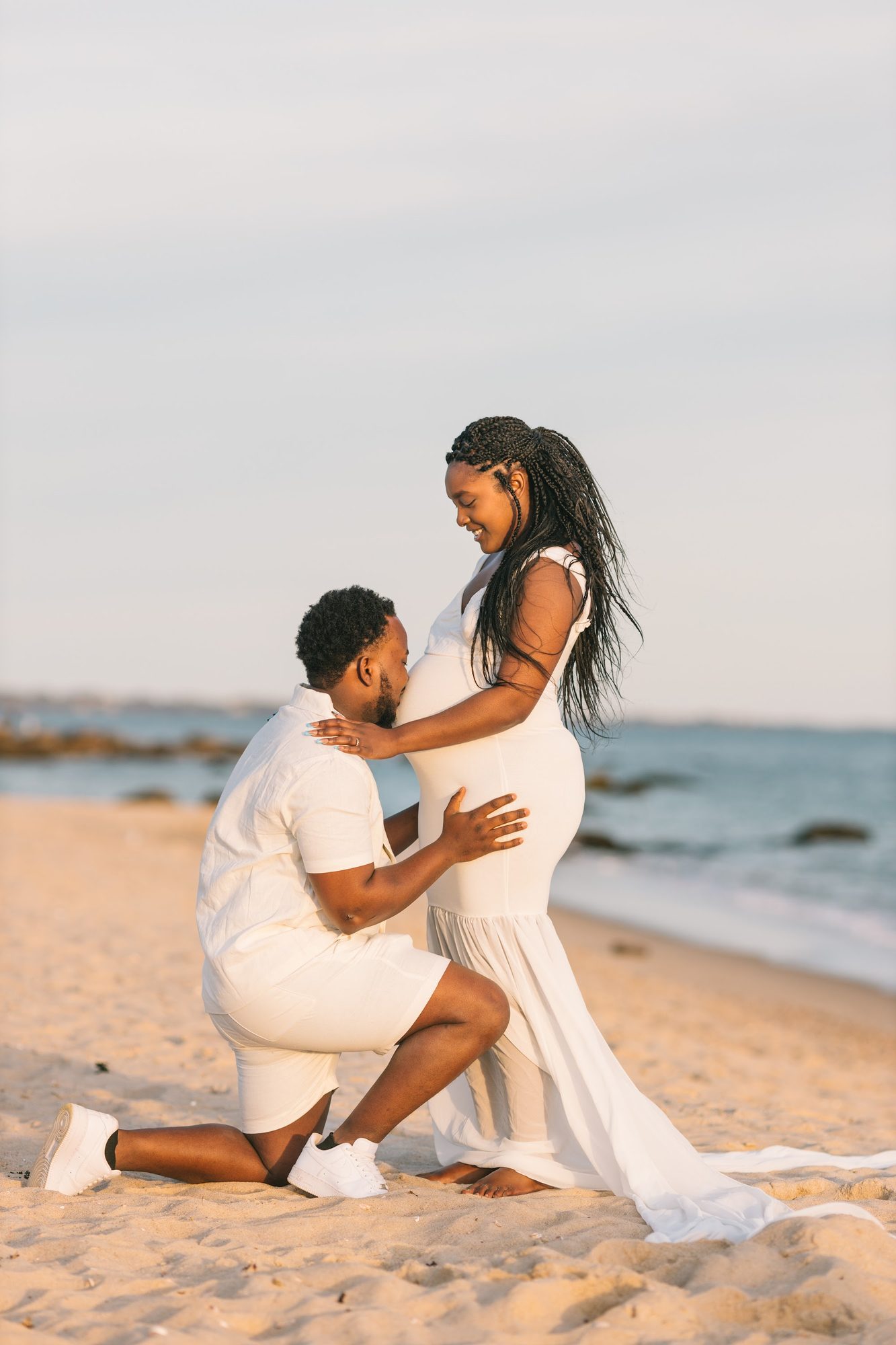 Partner kneeling to kiss the bump — beach maternity session