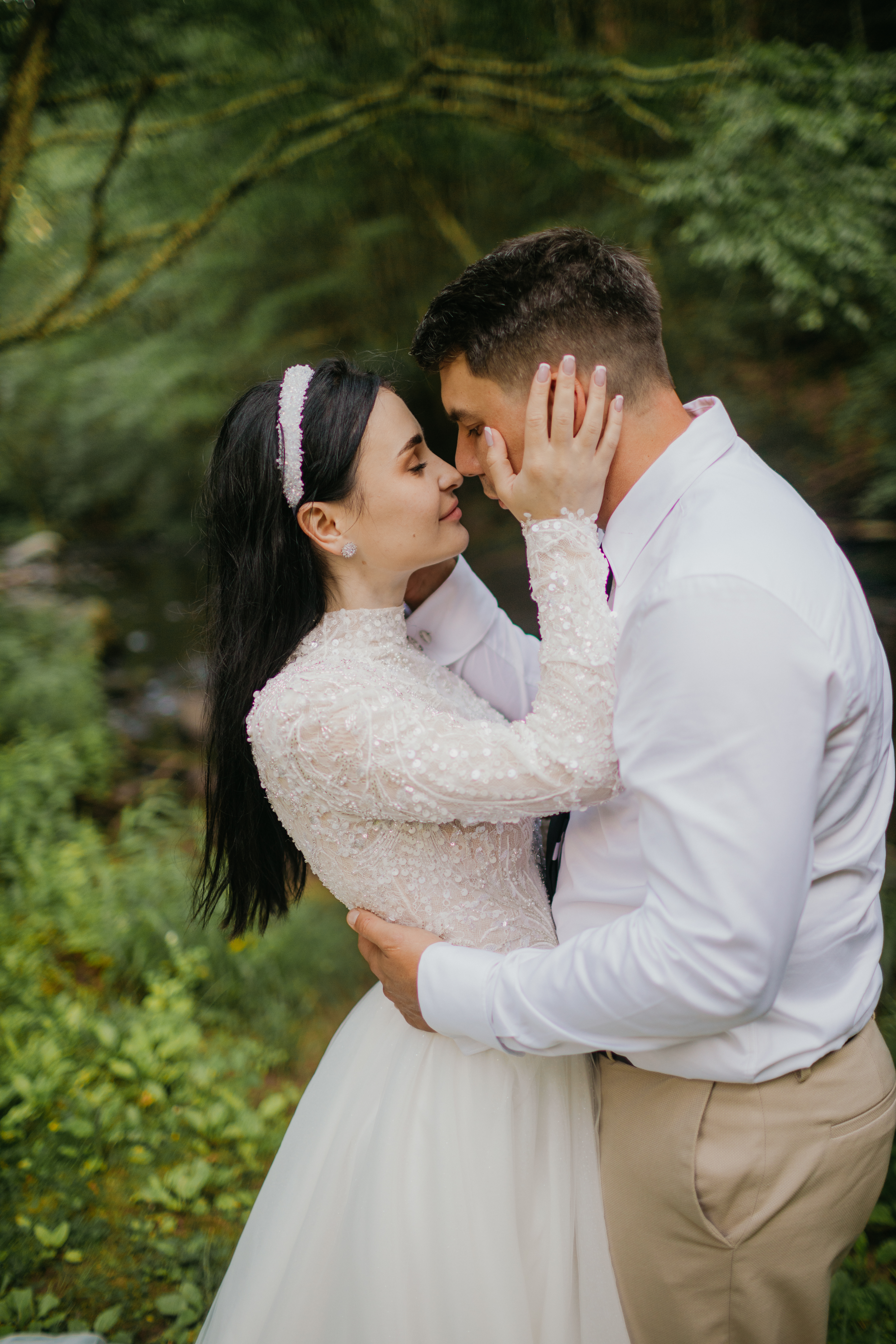 Bride and groom share an intimate kiss framed by forest greenery