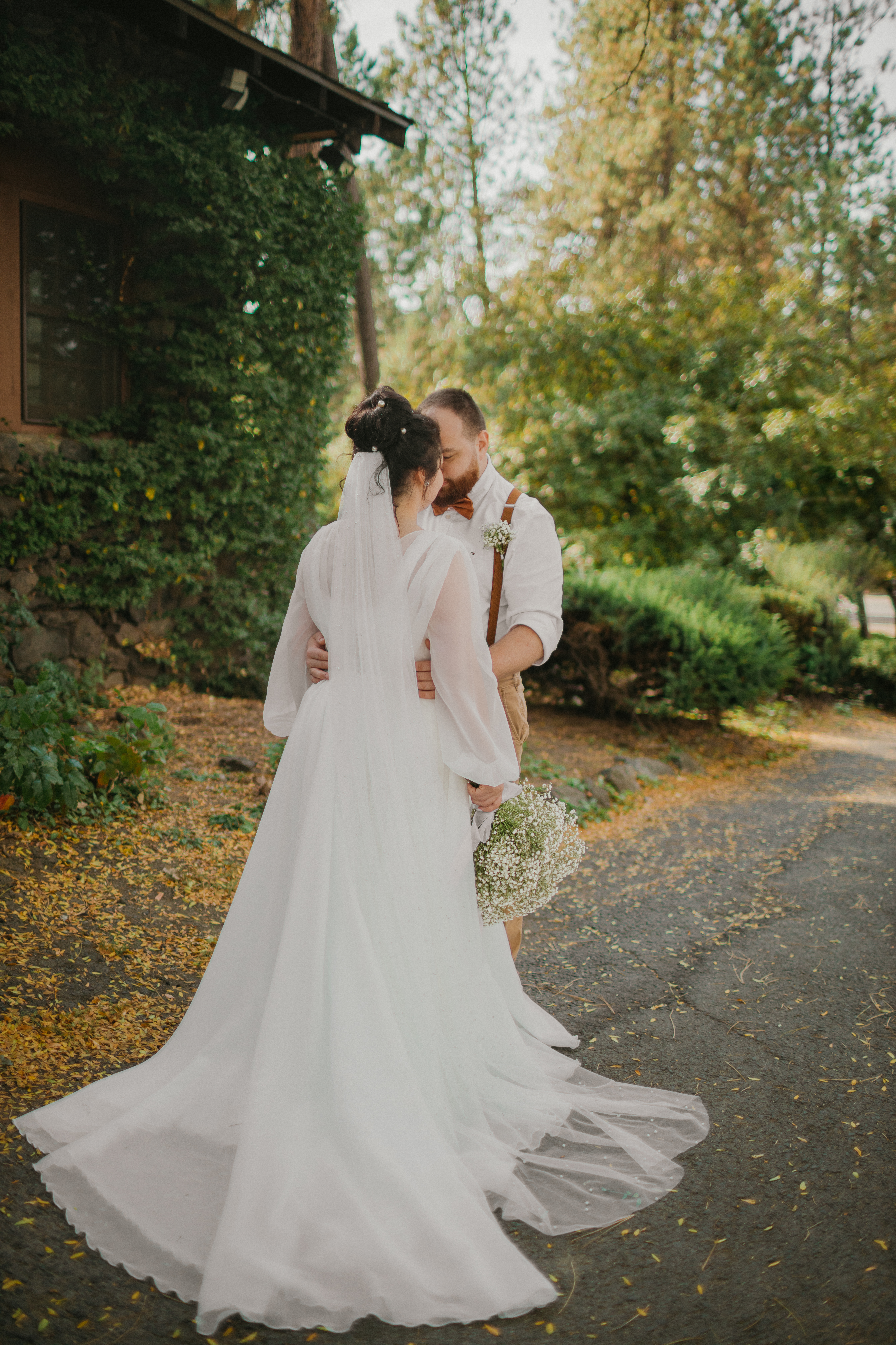 Bride and groom share a quiet kiss on a garden path in autumn light