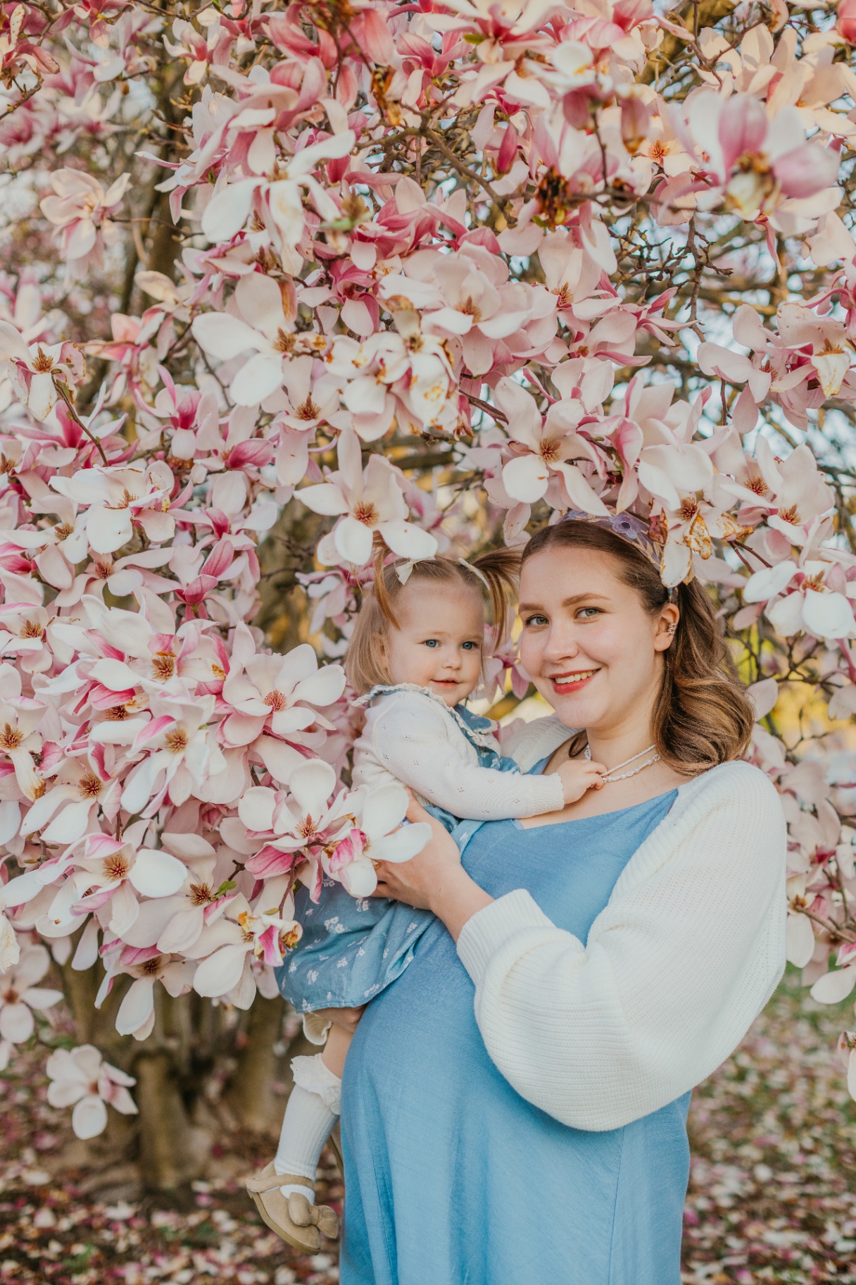 Mother holding daughter beneath a magnolia tree in spring bloom