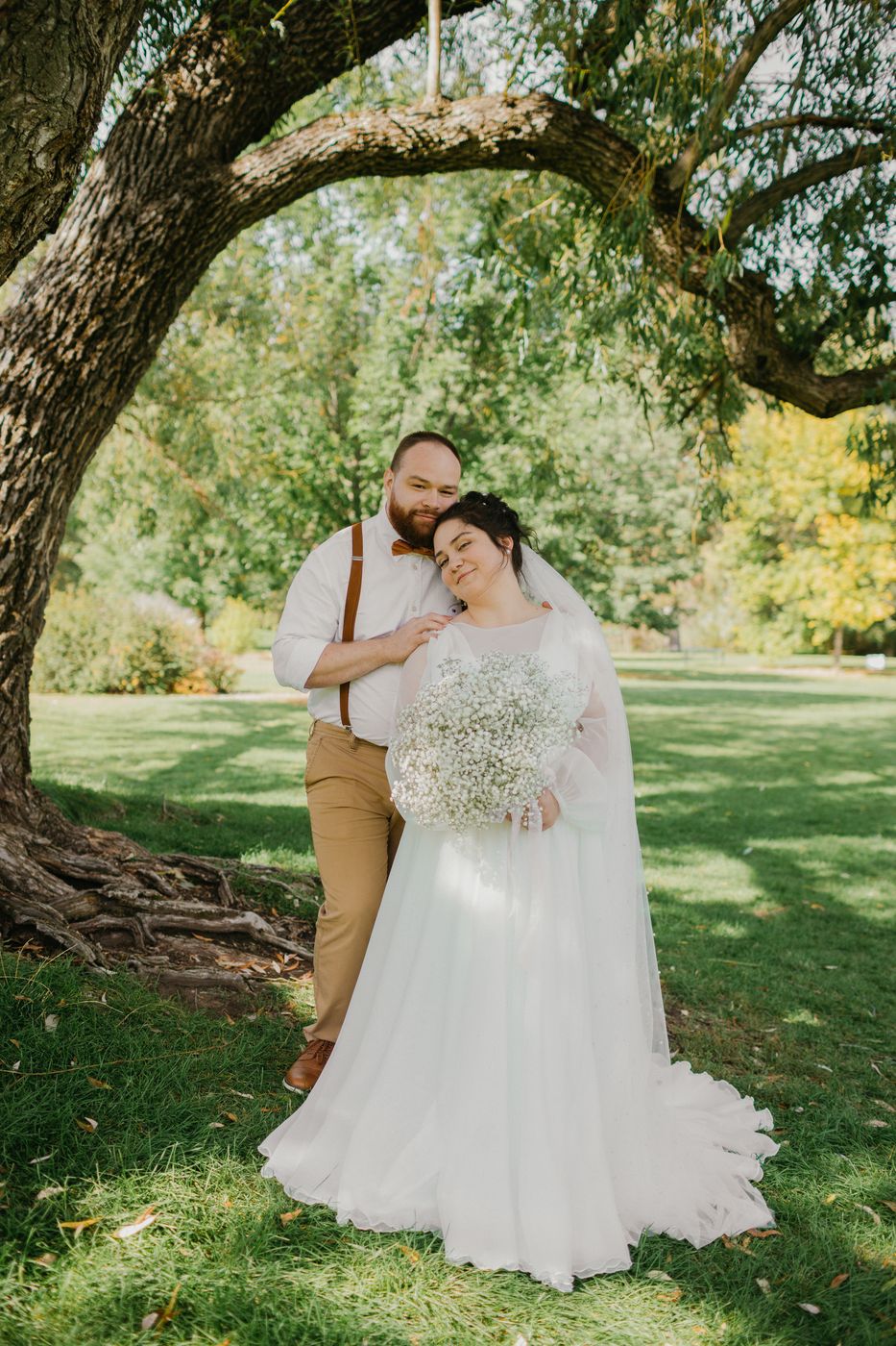 Bride and groom laughing beneath a willow tree with baby's breath bouquet